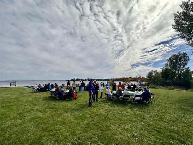 A group of people sitting around tables in the grass.